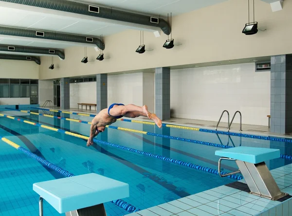 Joven nadador muscular saltando desde el bloque de partida en una piscina —  Fotos de Stock