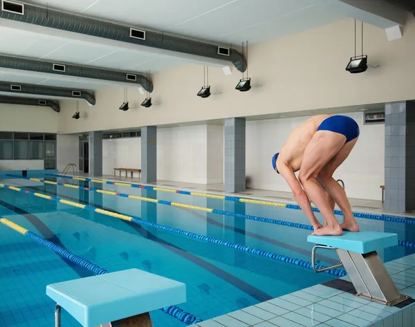 Junge muskulöse Schwimmerin in niedriger Position auf dem Startblock im Schwimmbad — Stockfoto