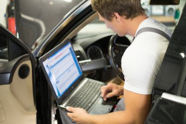 Serviceman making car diagnostics with laptop in a workshop clipart
