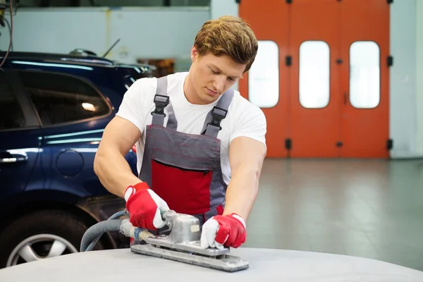 Junge Servicekräfte schleifen mit der Maschine auf der Motorhaube in einer Werkstatt — Stockfoto