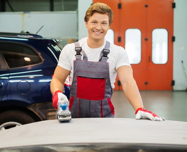 Unga serviceman utför slipning med maskin på en bil motorhuven i en workshop — Stockfoto