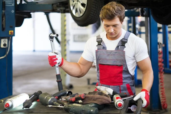 Jovem mecânico com ferramentas em uma oficina de carro — Fotografia de Stock