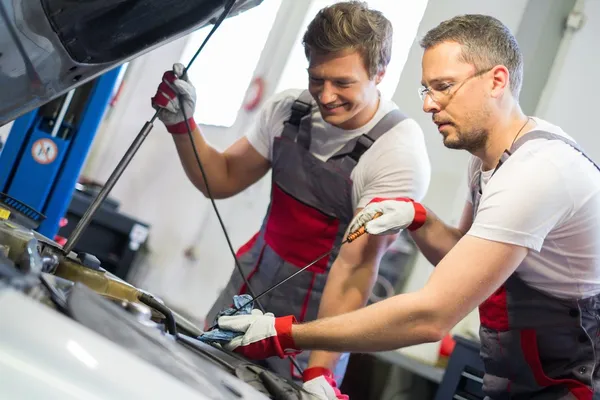 Dos mecánicos revisando el nivel de aceite en un taller de automóviles — Foto de Stock