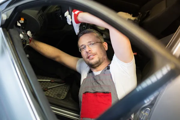 Fröhlicher Mechaniker mit Schraubenschlüssel, der irgendetwas im Autoinnenraum fixiert — Stockfoto