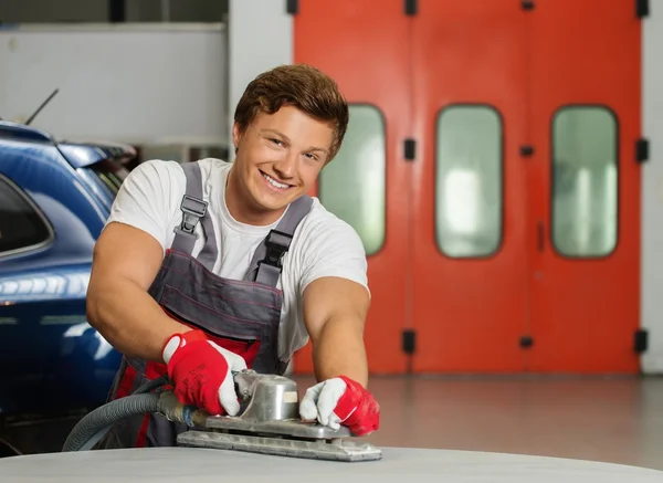 Junge Servicekräfte schleifen mit der Maschine auf der Motorhaube in einer Werkstatt — Stockfoto