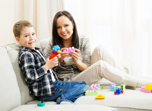 Glückliche junge Mutter mit ihrem Sohn auf einem Sofa, das mit einem Baukasten spielt — Stockfoto