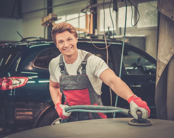 Serviceman performing grinding with machine on a car bonnet in a workshop — Stock Photo, Image