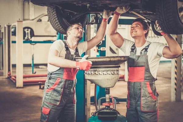 Two mechanics changing oil  in a car workshop — Stock Photo, Image