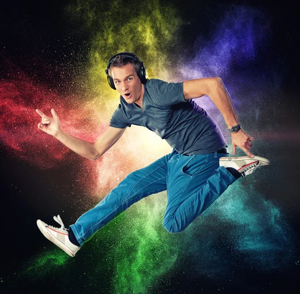 Handsome man with headphones jumping against colourful powder explosion — Stock Photo, Image