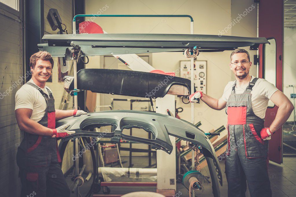 Two workers with car bodykit ready for painting in a Stock