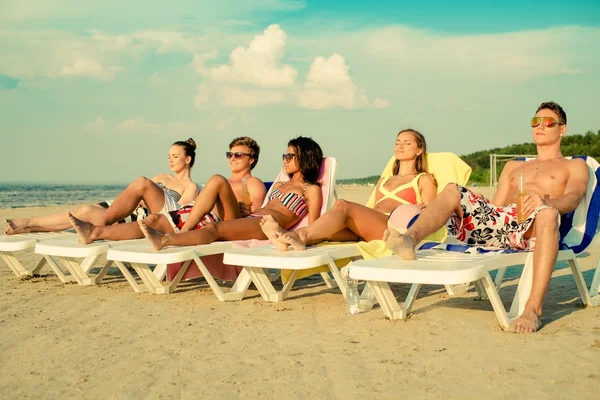 Grupo de amigos multiétnicos tomando el sol en una tumbona en una playa —  Fotos de Stock