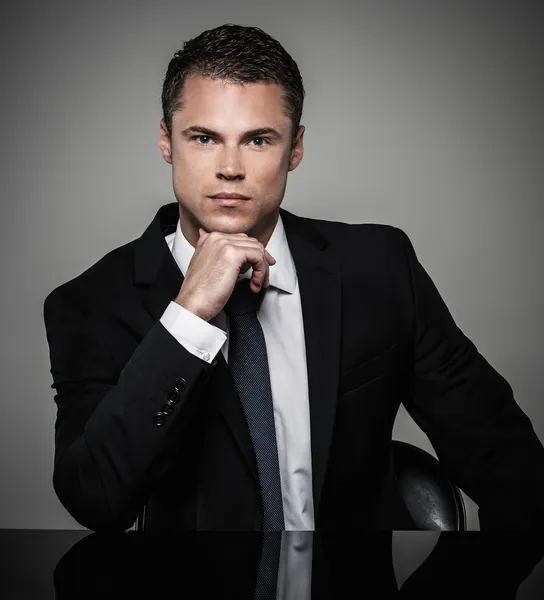 Guapo joven hombre bien vestido en chaqueta detrás de la mesa — Foto de Stock