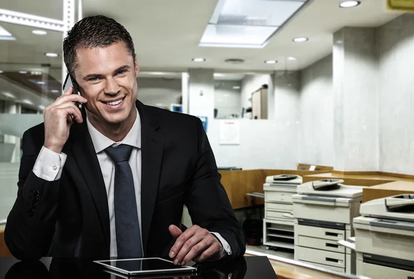 Schöner Mann im schwarzen Anzug mit Handy und Tablet-PC im modernen Büro — Stockfoto