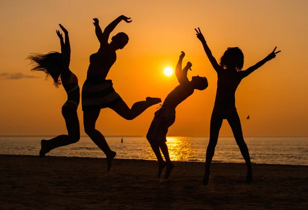 Siluetter en unga människor att ha kul på en strand mot solnedgången — Stockfoto