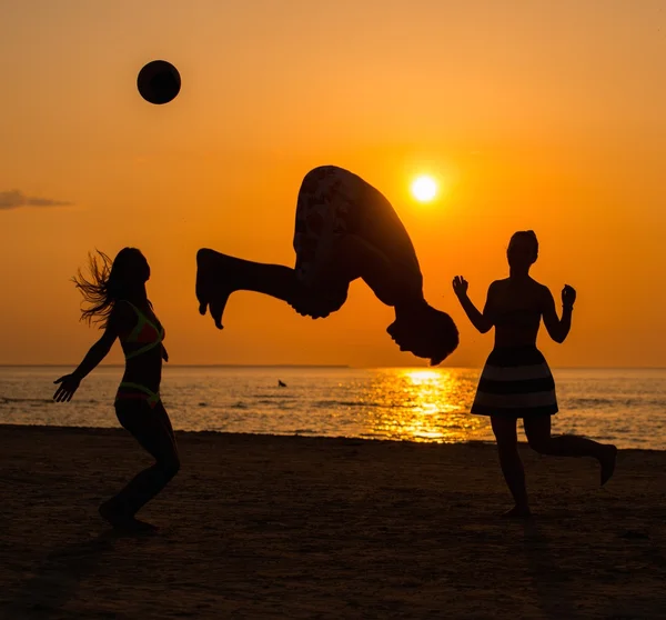 Siluetas a los jóvenes divirtiéndose en una playa contra el atardecer — Foto de Stock