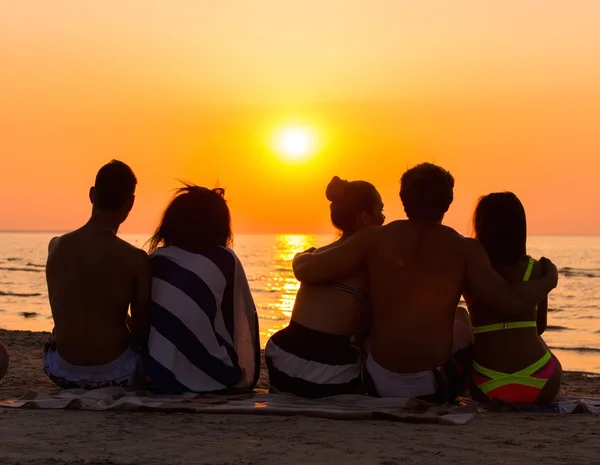 Silhouettes a young people sitting on a beach looking at  sunset — Stock Photo, Image