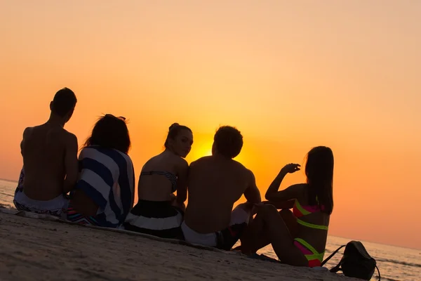 석양을 보고 해변에 앉아 젊은 사람들 실루엣 — 스톡 사진