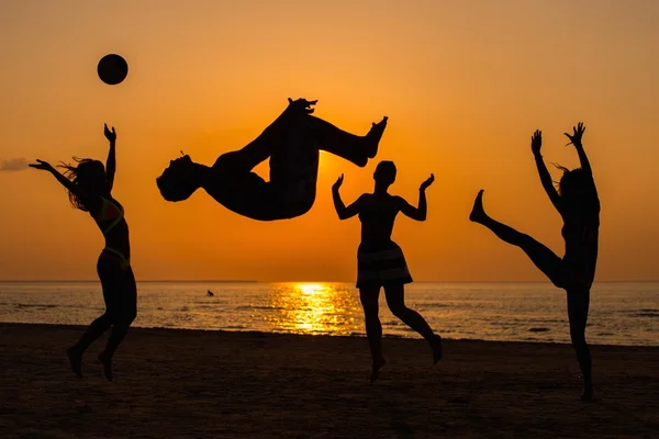 Silhuetas um jovem se divertindo em uma praia contra o pôr do sol — Fotografia de Stock