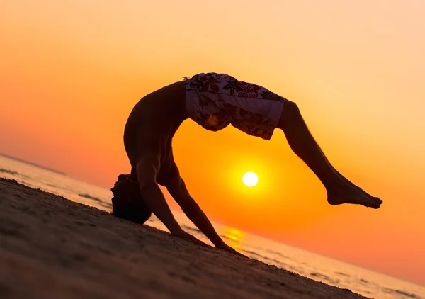 Sylwetki młody człowiek robi skoki na plaży przed zachodem słońca — Zdjęcie stockowe