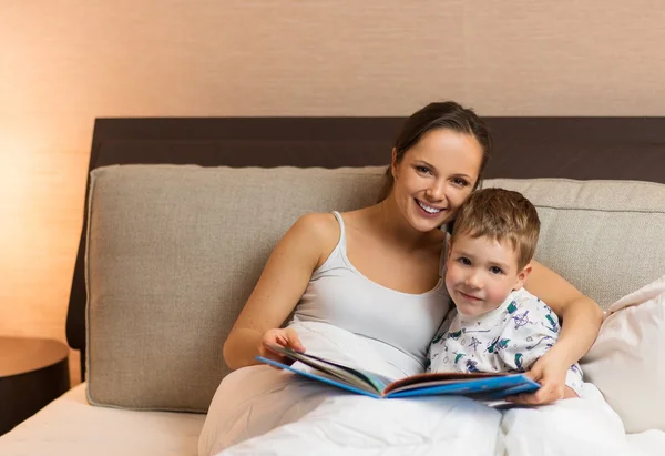 Mladá maminka a její syn, čtení knihy v posteli — Stock fotografie