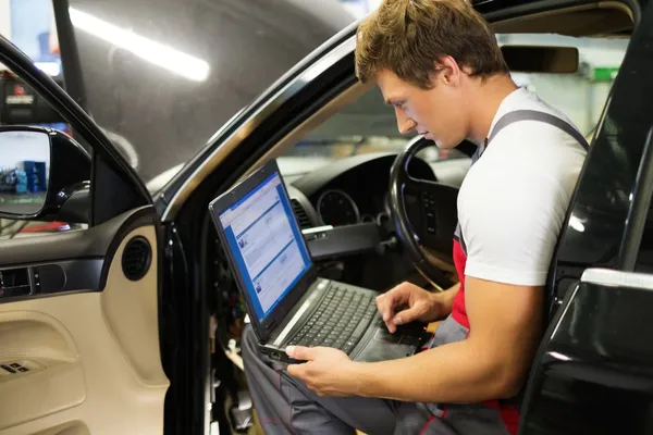 Serviceman fazendo diagnósticos de carro com laptop em uma oficina — Fotografia de Stock