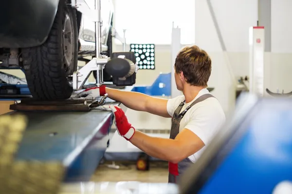 Young serviceman checking wheel alignment  in a car workshop — Stock Photo, Image