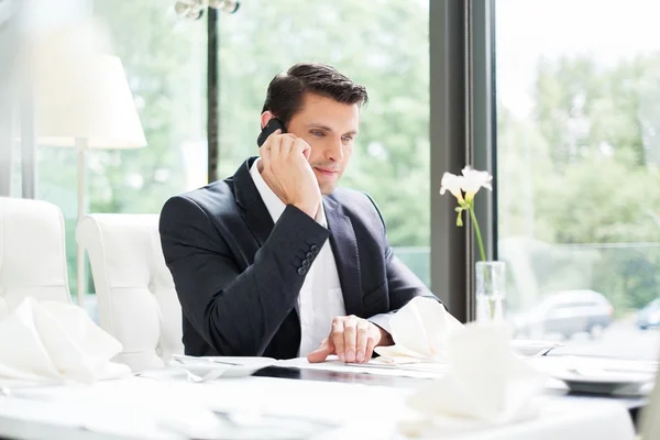 Knappe zakenman praten over mobiele telefoon in restaurant — Stockfoto