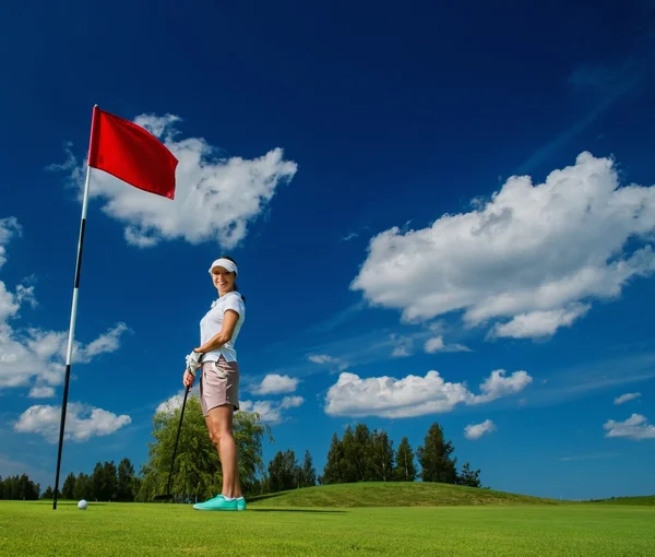 Mujer joven cerca del agujero con bandera roja en un campo de golf — Foto de Stock