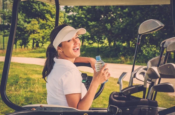En ung lystig kvinne med en flaske vann som kjører golfbil. – stockfoto