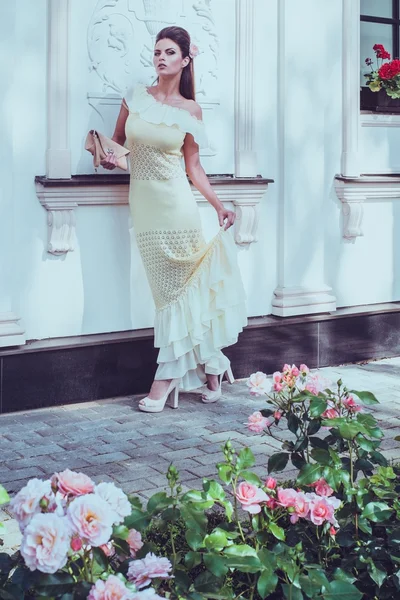 Красивая женщина в платье возле роскошного фасада здания среди роз — стоковое фото
