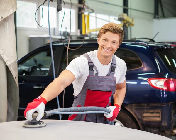 Junge Servicekräfte schleifen mit der Maschine auf der Motorhaube in einer Werkstatt — Stockfoto