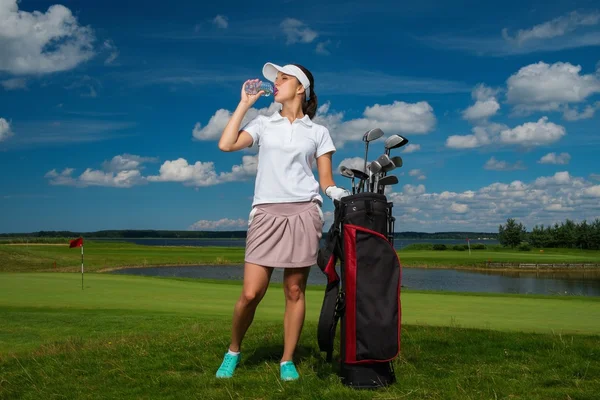 En ung kvinne som drikker vann på en golfbane. – stockfoto
