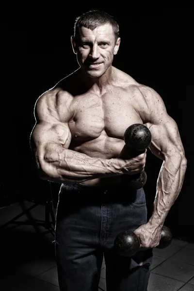 Gespierde man is aan te tonen zijn biceps terwijl hij dum houdt — Stockfoto