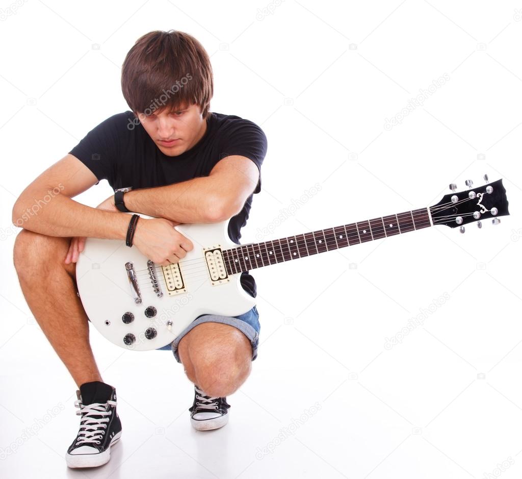 Sad teenage boy is squatting and holding his guitar