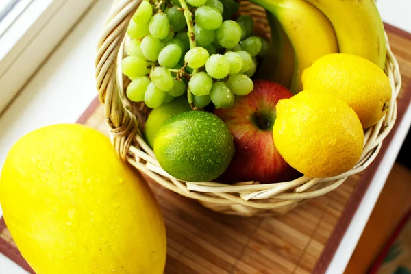 Saftige Früchte in Korb und Mango auf der Fensterbank — Stockfoto