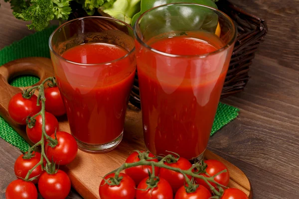 Dos vasos de jugo en una tabla de cortar y tomates —  Fotos de Stock