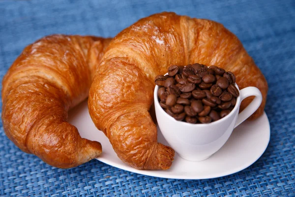 Två croissanter och kaffe bönor i en liten kopp — Stockfoto