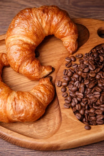 Croissants y granos de café en una tabla de madera — Foto de Stock