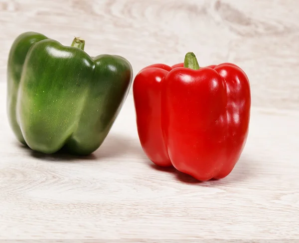 Um verde e um pimentão vermelho em madeira clara — Fotografia de Stock