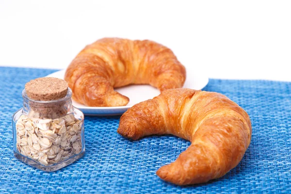 Two croissants on a blue cloth and a jar with oats — Stock Photo, Image