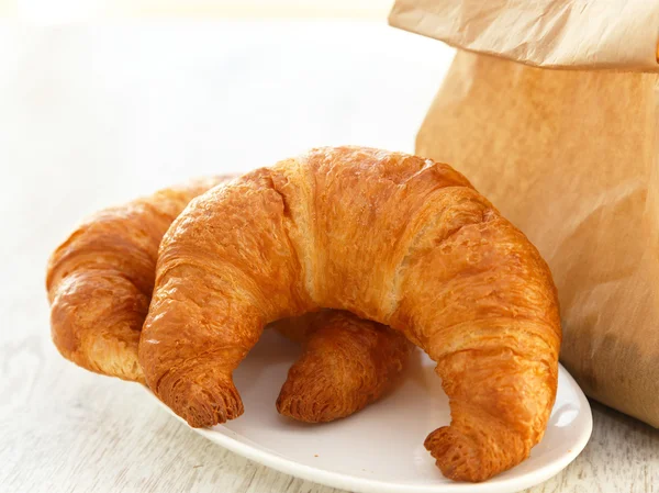Två croissanter på en tallrik och en papperspåse — Stockfoto