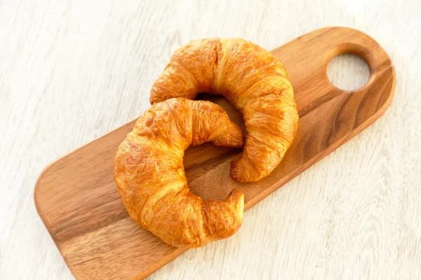 Dois croissants em uma placa de corte de madeira — Fotografia de Stock