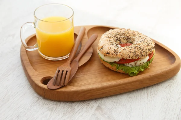 A bun sandwich and juice on a wooden plate — Stock Photo, Image