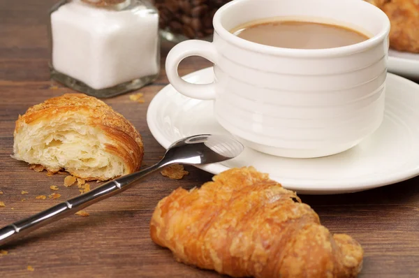 Half-gegeten croissant en kruimels door een kopje koffie — Stockfoto