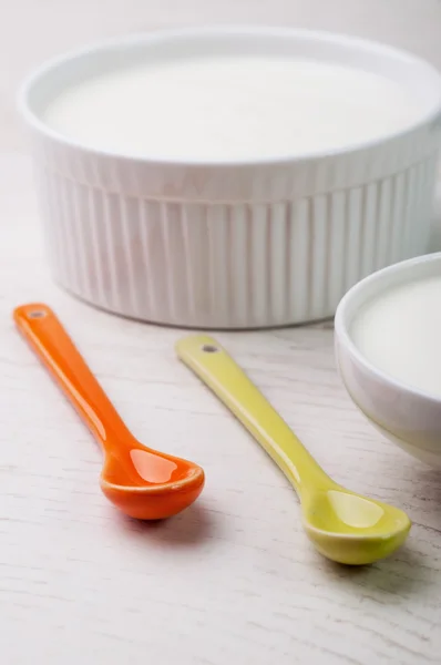 An orange and a yellow spoon and a bowl of yogurt — Stock Photo, Image