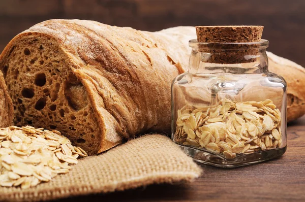 Una barra de pan crujiente y un frasco de avena —  Fotos de Stock