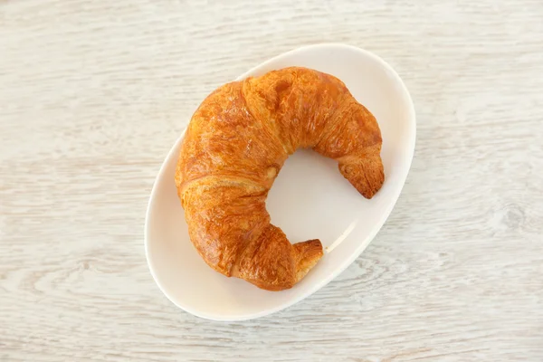 One croissant on a white plate on wooden surface — Stock Photo, Image