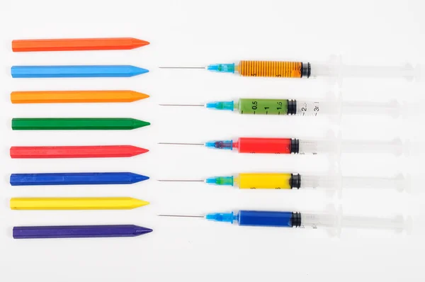 Colorful syringes and same color crayons pointing at each other — Stock Photo, Image