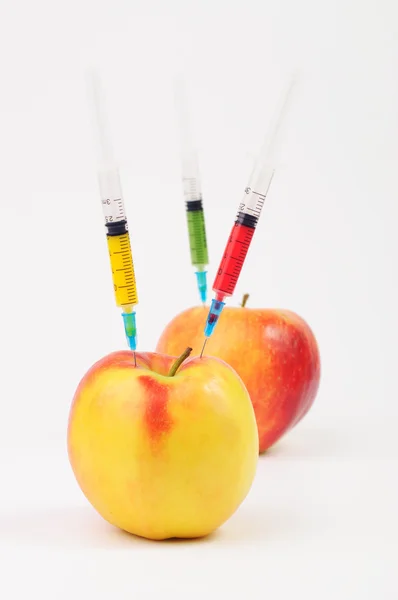 Three color syringes sticking out of two apples — Stock Photo, Image