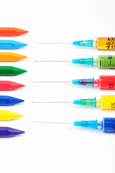 Jeringas coloridas apuntando a los mismos crayones de color — Foto de Stock